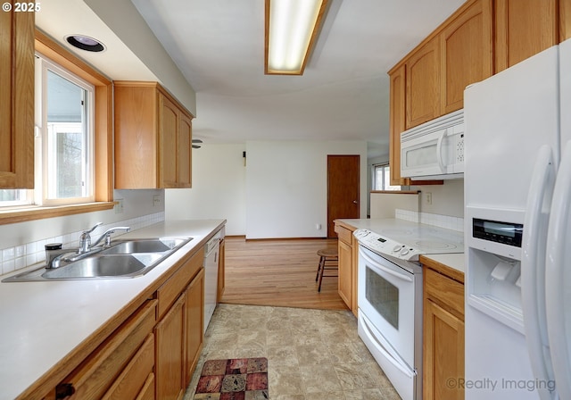 kitchen with a sink, baseboards, white appliances, and light countertops