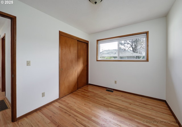 unfurnished bedroom featuring visible vents, light wood-style flooring, baseboards, and a closet