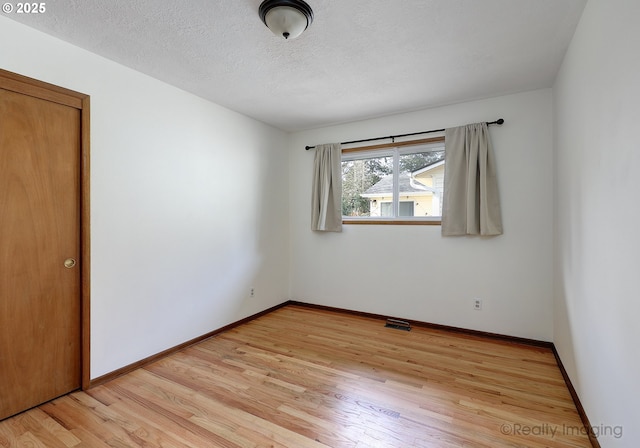 spare room with visible vents, light wood-style flooring, a textured ceiling, and baseboards