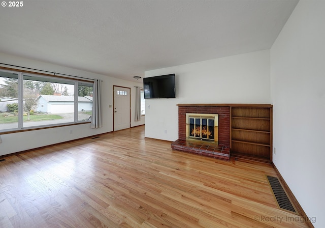 unfurnished living room featuring visible vents, light wood-style flooring, a brick fireplace, and baseboards