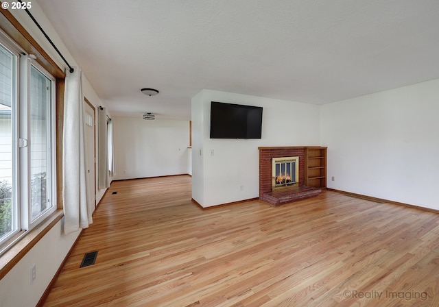 unfurnished living room featuring visible vents, a fireplace, light wood-type flooring, and baseboards