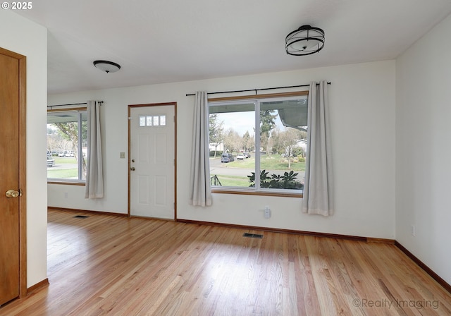 foyer entrance with light wood-style flooring, baseboards, and visible vents