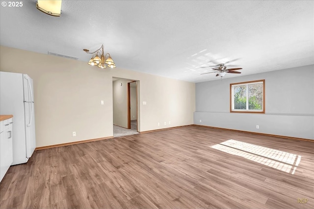 spare room with a textured ceiling, ceiling fan with notable chandelier, visible vents, and light wood-style floors