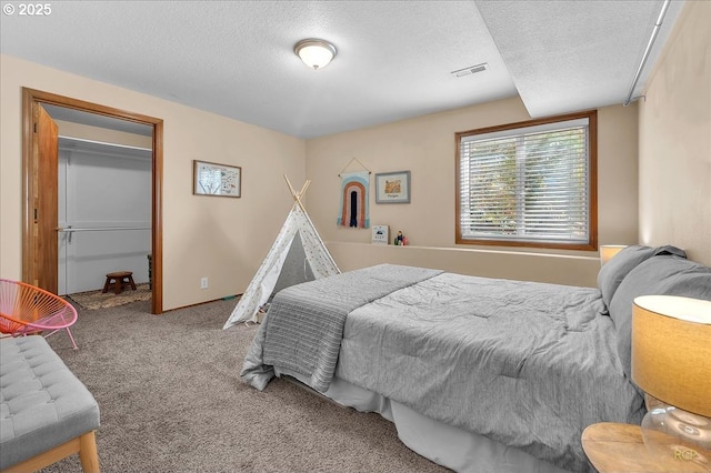 carpeted bedroom featuring visible vents, a textured ceiling, and a spacious closet