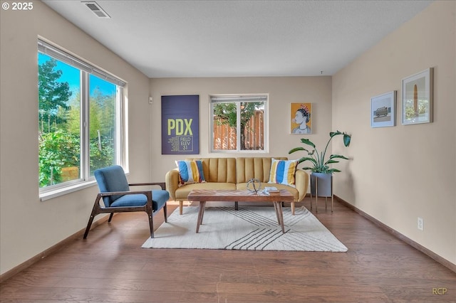 living area featuring a healthy amount of sunlight, visible vents, baseboards, and wood finished floors