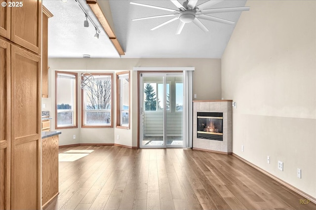 unfurnished living room with a fireplace, wood finished floors, a ceiling fan, and track lighting