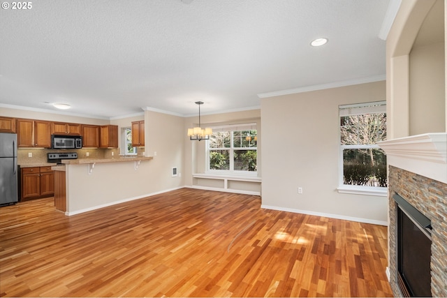 unfurnished living room featuring baseboards, a fireplace, ornamental molding, light wood-style floors, and a notable chandelier