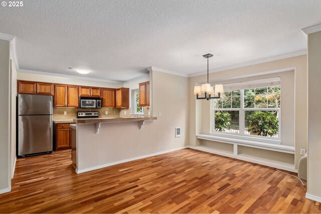 kitchen with a notable chandelier, wood finished floors, appliances with stainless steel finishes, brown cabinetry, and decorative backsplash