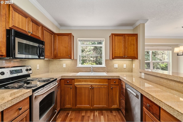 kitchen with brown cabinets, a sink, tile countertops, stainless steel appliances, and a healthy amount of sunlight