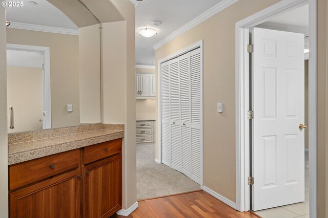 hallway featuring light wood-type flooring, arched walkways, baseboards, and ornamental molding