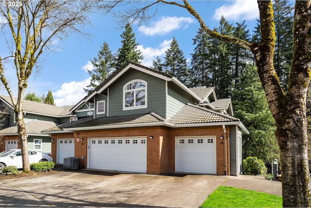 view of front of house featuring brick siding, a tile roof, cooling unit, a garage, and driveway