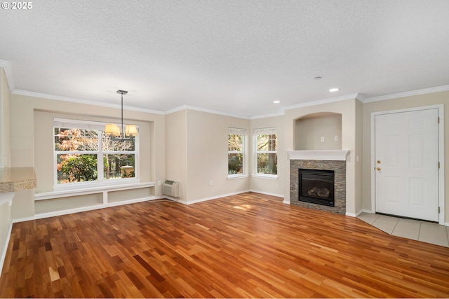unfurnished living room with a stone fireplace, a notable chandelier, a healthy amount of sunlight, and light wood-style flooring