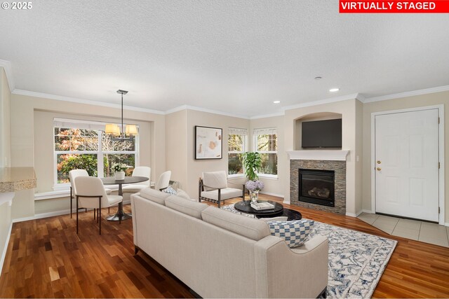 living area featuring wood finished floors, a textured ceiling, a glass covered fireplace, crown molding, and a chandelier