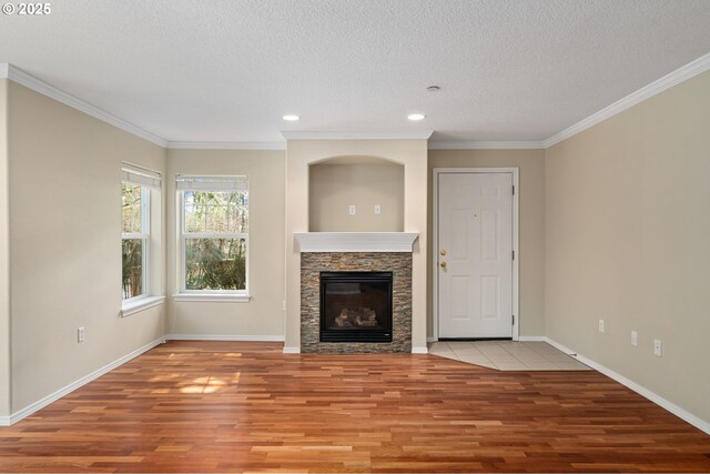 unfurnished living room with a fireplace, a textured ceiling, baseboards, and wood finished floors