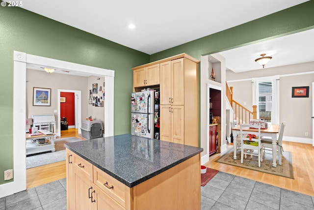 kitchen featuring dark stone countertops, a kitchen island, light tile patterned flooring, light brown cabinets, and stainless steel fridge