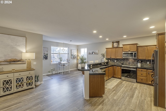 kitchen with dark countertops, a sink, brown cabinets, a peninsula, and appliances with stainless steel finishes