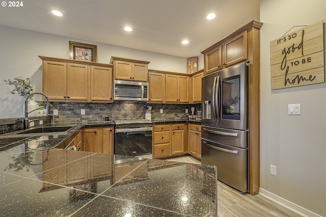 kitchen featuring light wood finished floors, a sink, baseboards, backsplash, and appliances with stainless steel finishes