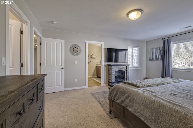 bedroom with visible vents, light carpet, ensuite bath, baseboards, and a fireplace