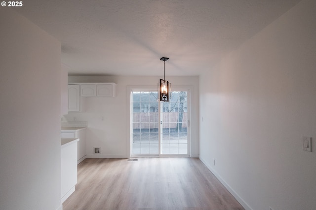 unfurnished dining area with a chandelier, a textured ceiling, and light wood-type flooring