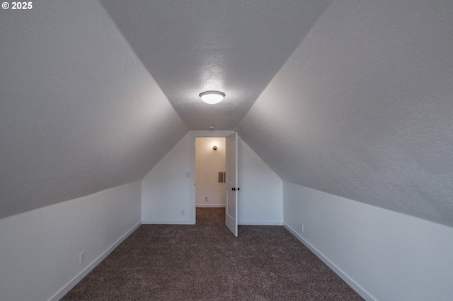 additional living space with lofted ceiling, a textured ceiling, and dark colored carpet