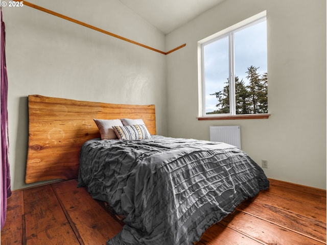 bedroom with wood-type flooring, radiator heating unit, and vaulted ceiling
