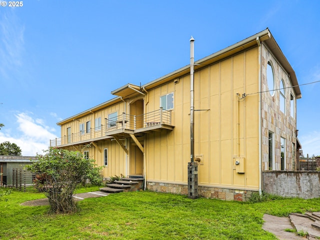 back of house with a lawn, board and batten siding, and a balcony