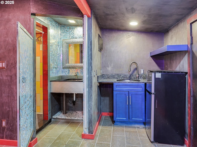 bar with a sink, baseboards, freestanding refrigerator, and indoor wet bar