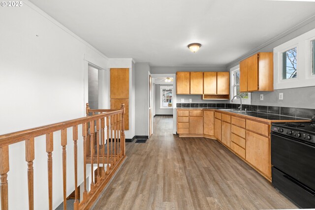 kitchen with black range oven, sink, crown molding, light brown cabinets, and light wood-type flooring