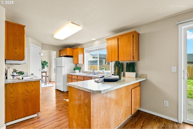 kitchen featuring freestanding refrigerator, light wood-type flooring, light countertops, a sink, and a peninsula