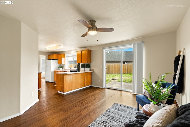 kitchen featuring freestanding refrigerator, a peninsula, brown cabinets, light countertops, and dark wood-style floors