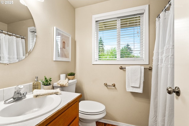 bathroom with toilet, vanity, wood finished floors, and baseboards