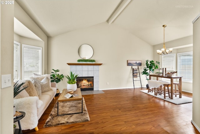 living room featuring wood finished floors, a tile fireplace, a chandelier, beam ceiling, and baseboards