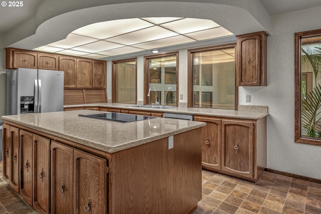 kitchen with arched walkways, black electric stovetop, a sink, a kitchen island, and baseboards