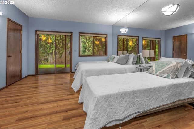 bedroom featuring access to outside, multiple windows, a textured ceiling, and wood finished floors