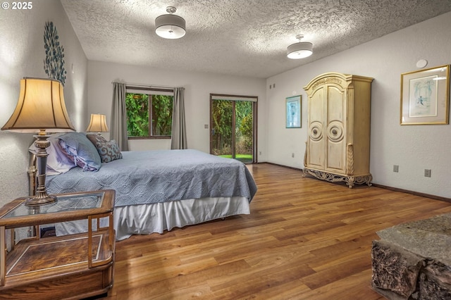 bedroom featuring a textured ceiling, a textured wall, wood finished floors, baseboards, and access to outside