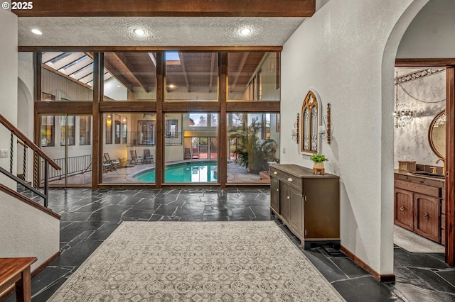 interior space with arched walkways, stone tile flooring, a textured wall, and baseboards