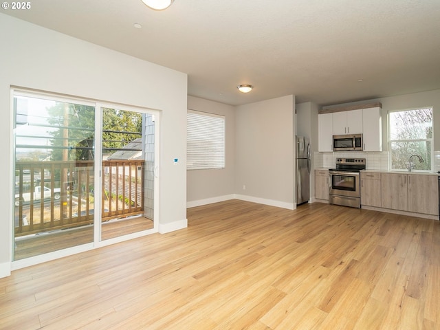 kitchen with light wood finished floors, white cabinets, stainless steel appliances, light countertops, and backsplash