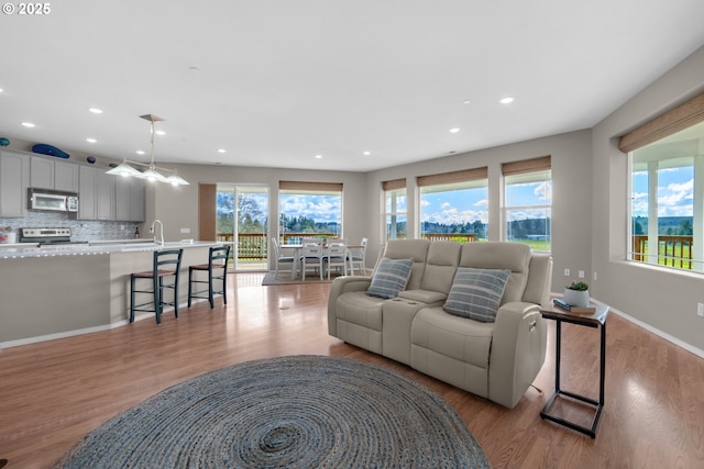 living area featuring baseboards, light wood finished floors, recessed lighting, and a healthy amount of sunlight