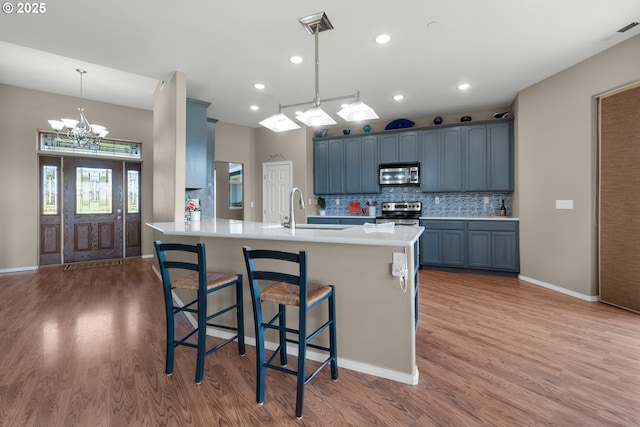 kitchen with backsplash, appliances with stainless steel finishes, light wood-style floors, a sink, and a kitchen breakfast bar