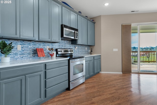 kitchen featuring stainless steel appliances, wood finished floors, backsplash, and light countertops