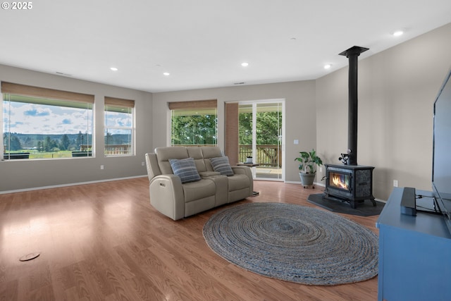 living room with recessed lighting, a wood stove, baseboards, and wood finished floors