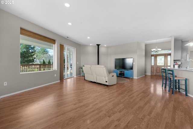 living area featuring a notable chandelier, recessed lighting, a wood stove, light wood-type flooring, and baseboards