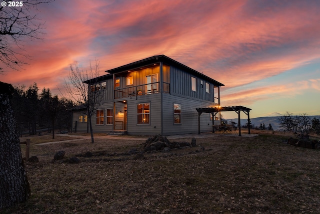 back of house at dusk with board and batten siding, a patio area, a balcony, and a pergola