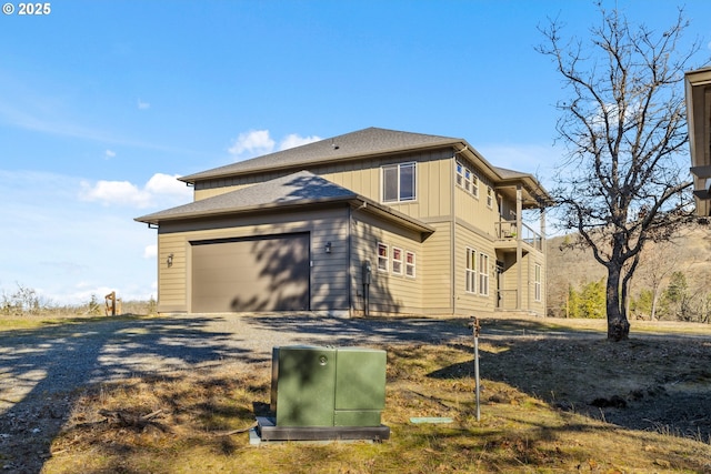 view of side of home with a garage, gravel driveway, a balcony, and board and batten siding