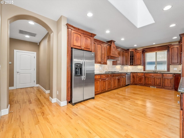1303 NE 147th Ave, Vancouver, WA 98684 - kitchen featuring appliances with stainless steel finishes, arched walkways, premium range hood, light wood-style floors, and tasteful backsplash