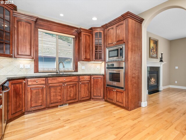 1303 NE 147th Ave, Vancouver, WA 98684 - kitchen featuring stainless steel appliances, a sink, light wood-style floors, arched walkways, and dark stone countertops