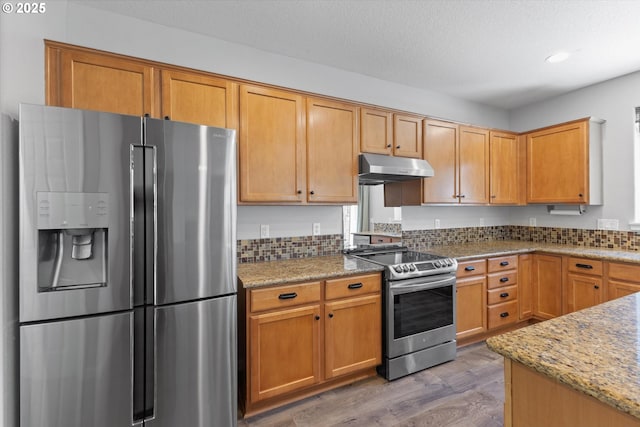 12800 Joys Dr, Oregon City, OR 97045 - kitchen with appliances with stainless steel finishes, under cabinet range hood, light wood finished floors, light stone counters, and decorative backsplash