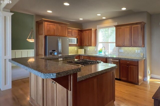 kitchen with stainless steel appliances, a sink, light wood-style flooring, brown cabinetry, and decorative backsplash