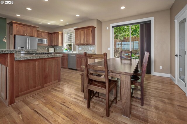 kitchen with appliances with stainless steel finishes, light wood-type flooring, tasteful backsplash, brown cabinetry, and recessed lighting