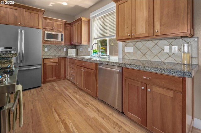 kitchen featuring appliances with stainless steel finishes, light wood finished floors, a sink, backsplash, and brown cabinetry